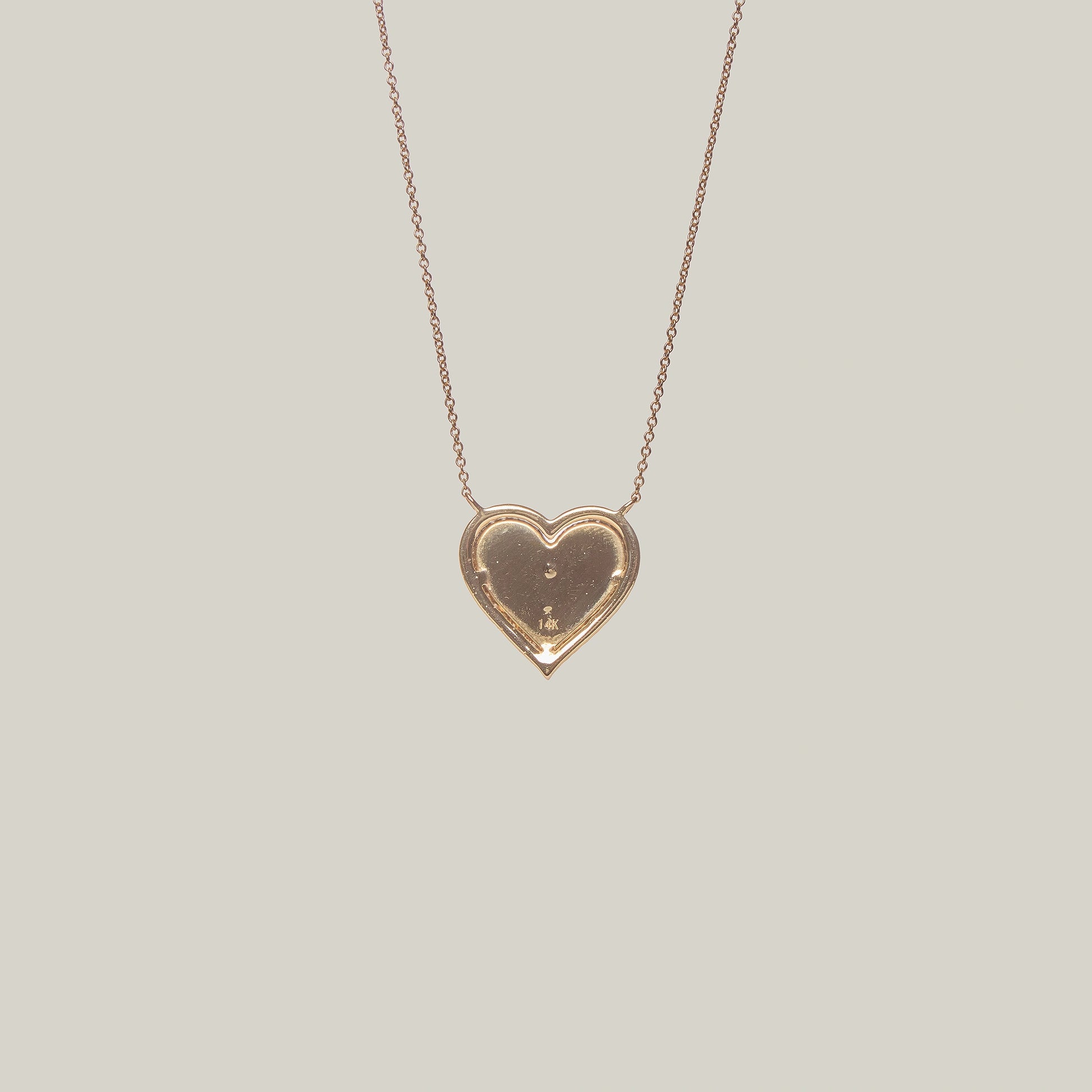 Close up rear view of a gold heart-shaped pendant with a diamond encrusted center and border on a light gray background