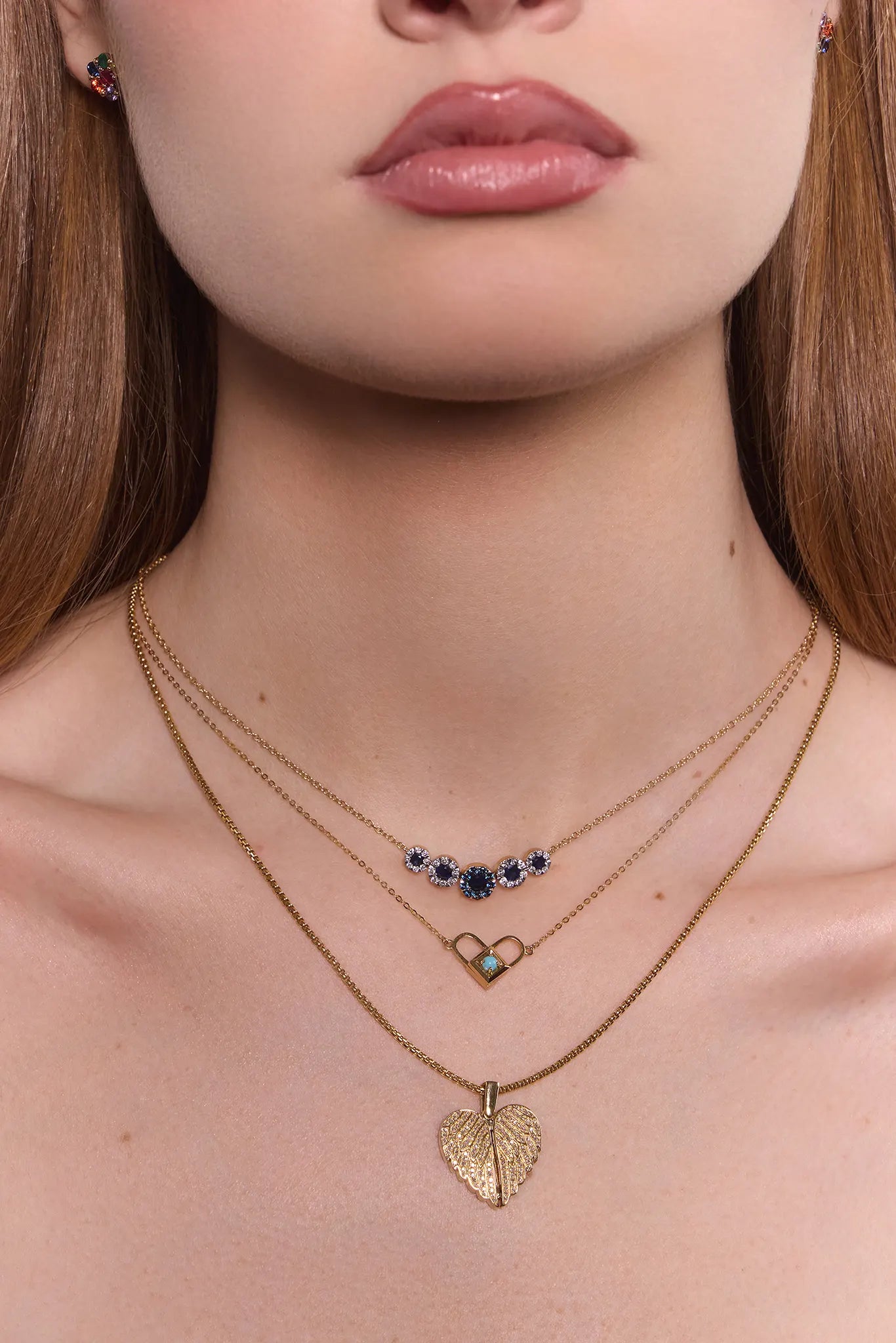 Close-up of a woman wearing gold necklaces with heart and blue gemstone pendants