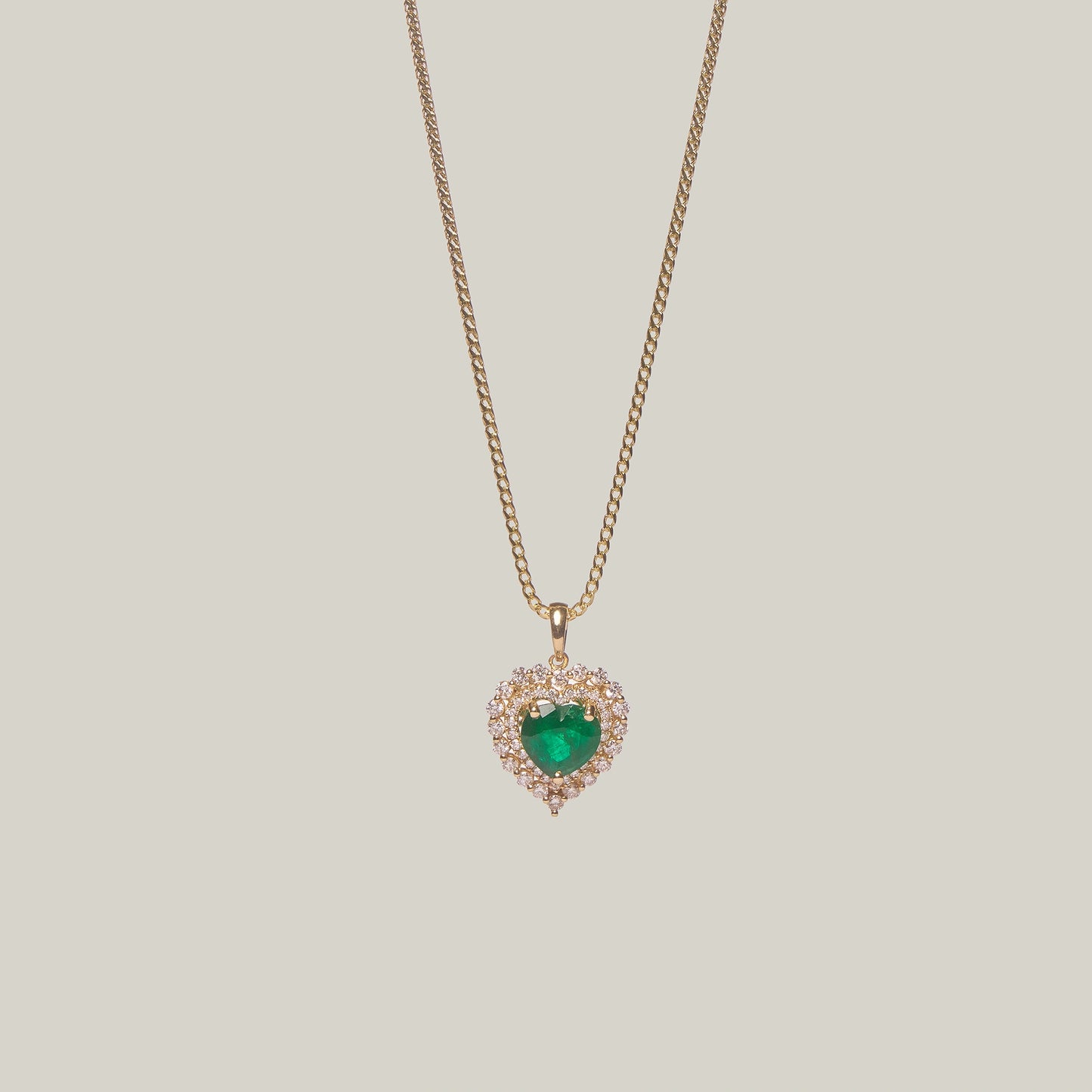 Front-facing close-up of a gold necklace with a heart-shaped emerald pendant on a light gray background