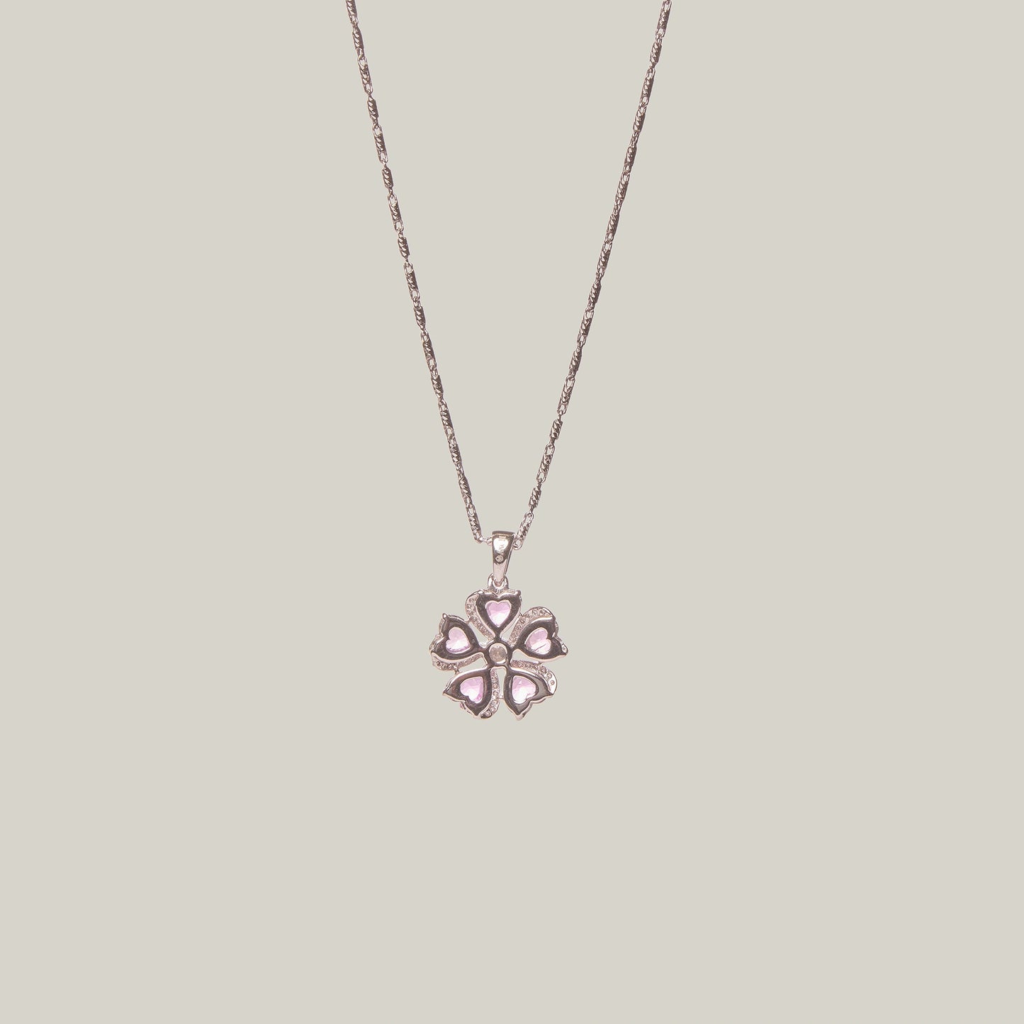 Reverse view of a necklace with a pink flower-shaped pendant on a light gray background