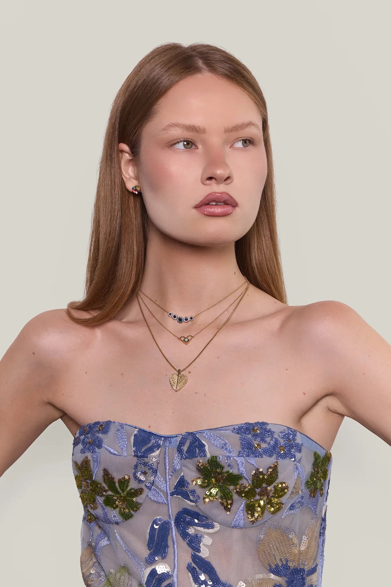 Woman wearing a strapless dress with floral patterns and layered necklaces against a plain background