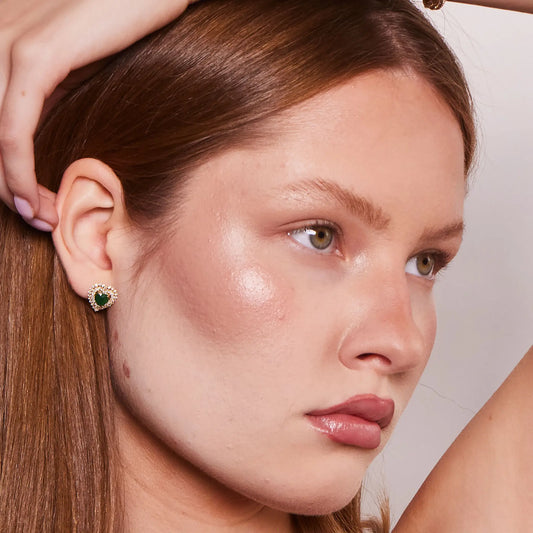 Close-up of a woman wearing a green gemstone earring and diamond tennis bracelet with a neutral background