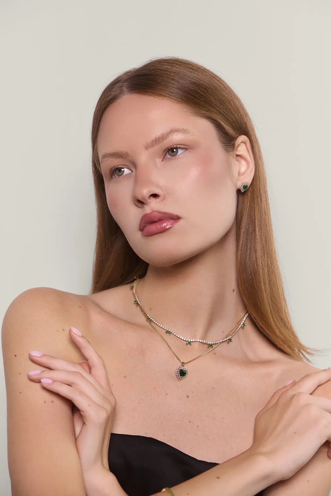 Woman wearing emerald earrings with a matching heart shaped necklace and a diamond tennis necklace
