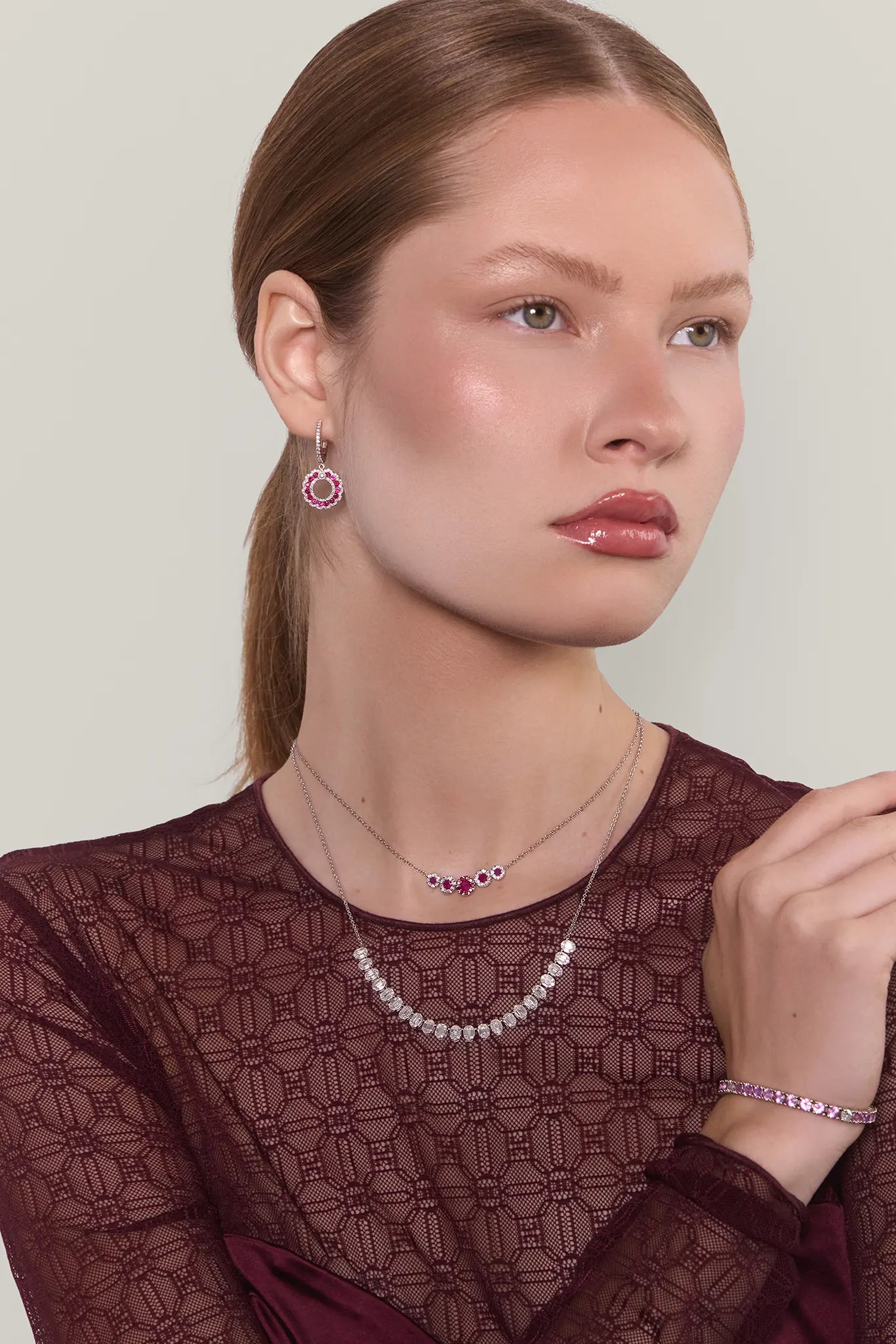 Woman wearing jewelry including earrings, a necklace, and a bracelet on a plain background