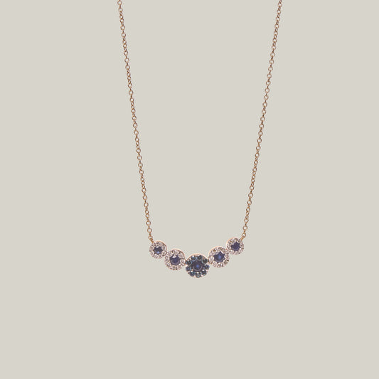 Gold necklace with blue sapphires and diamonds on a light gray background