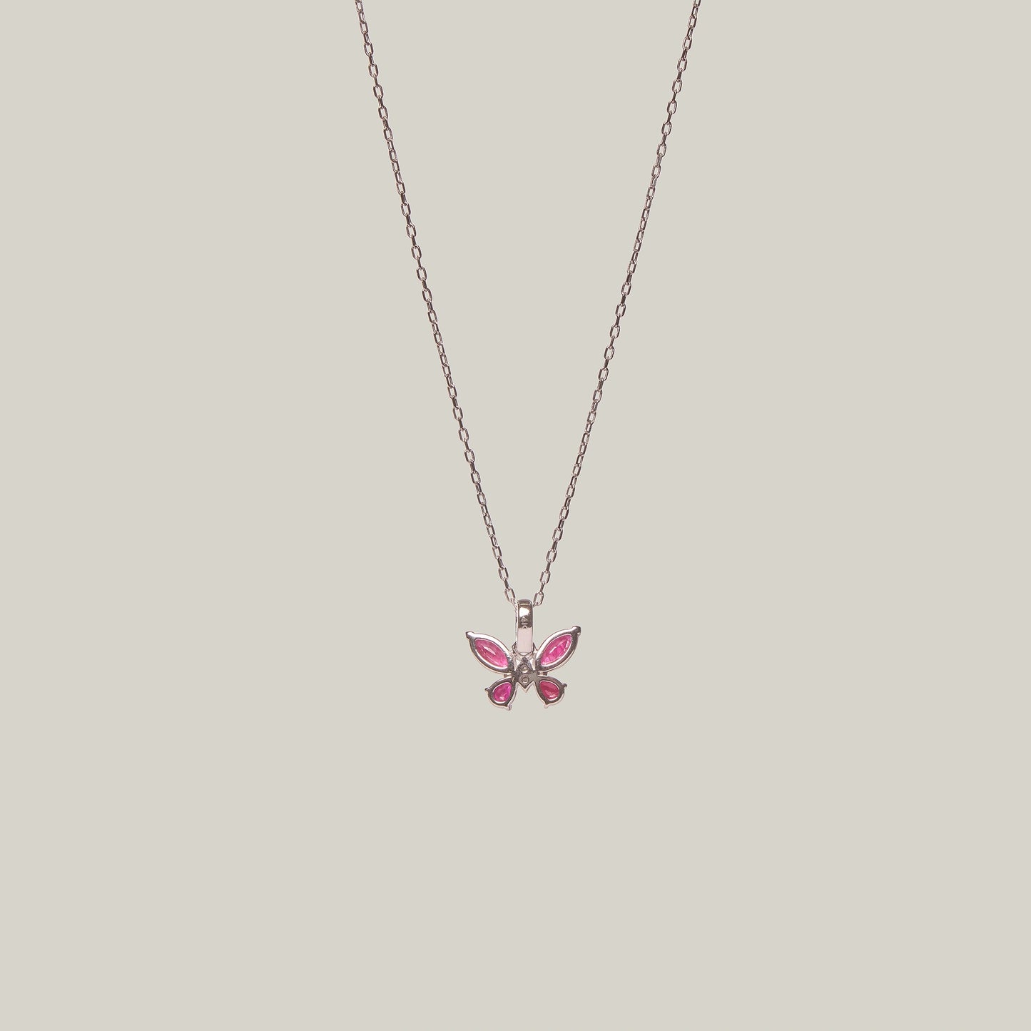 Reverse view of a butterfly-shaped pink pendant on a chain against a light gray background