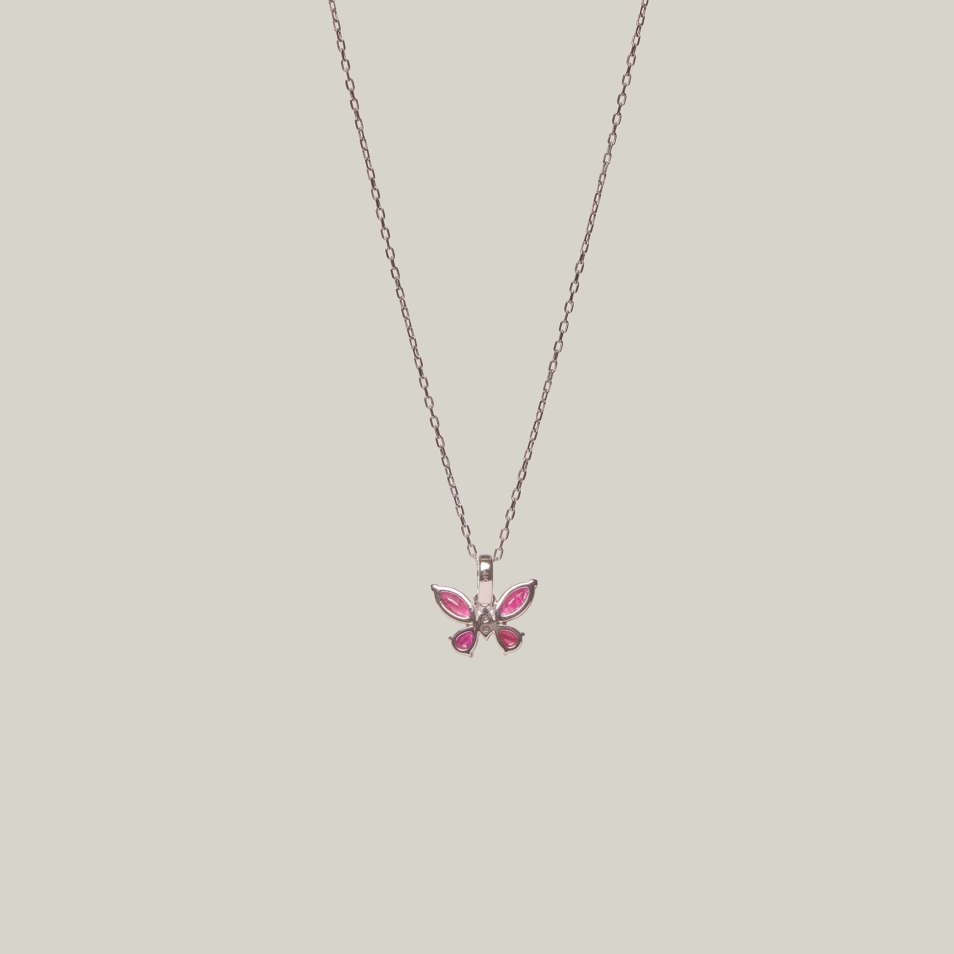 Reverse view of a butterfly-shaped pink pendant on a chain against a light gray background