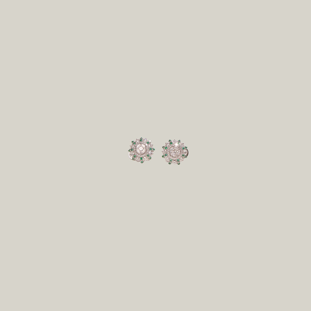Pair of diamond stud earrings with emerald accents on a light gray background