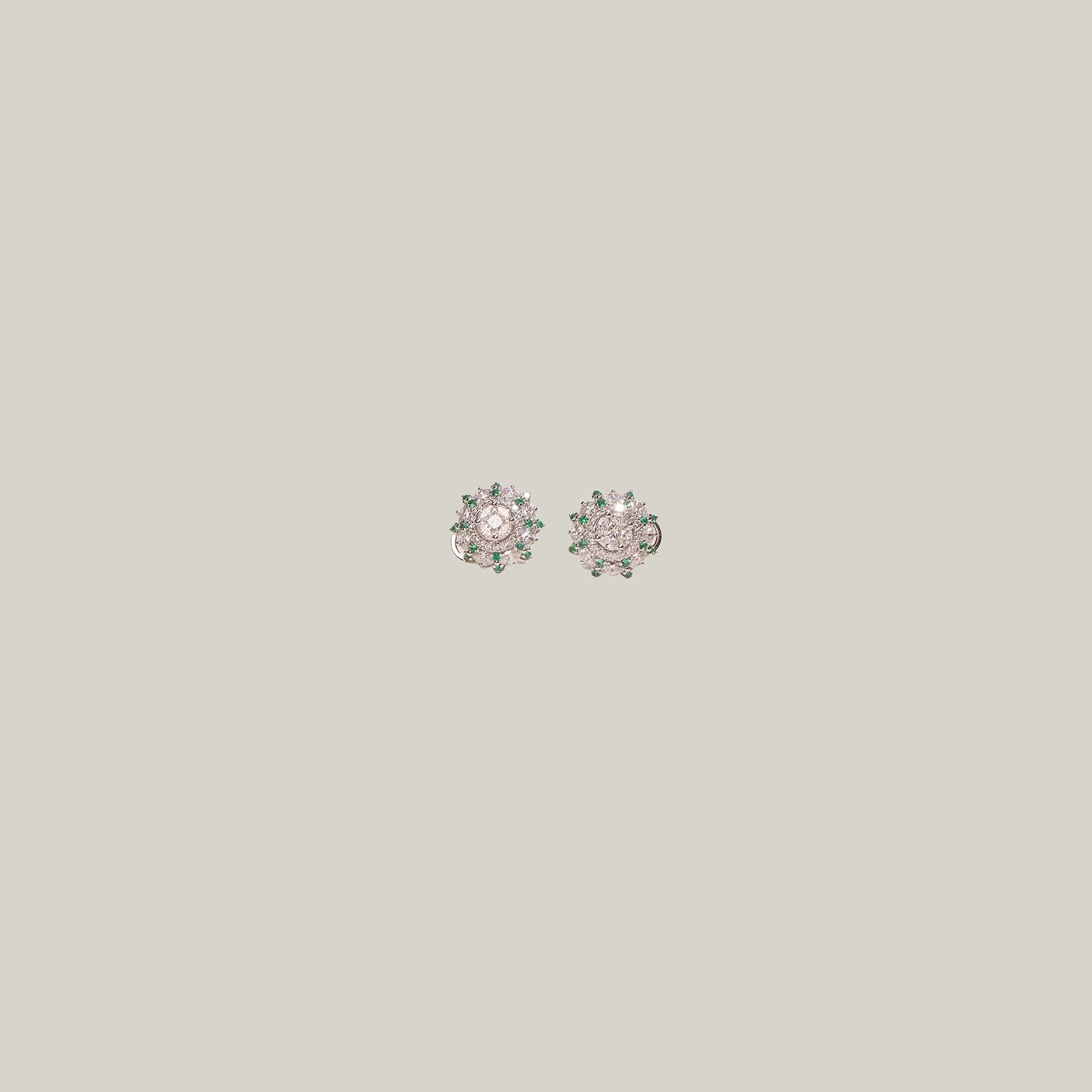 Pair of diamond stud earrings with emerald accents on a light gray background
