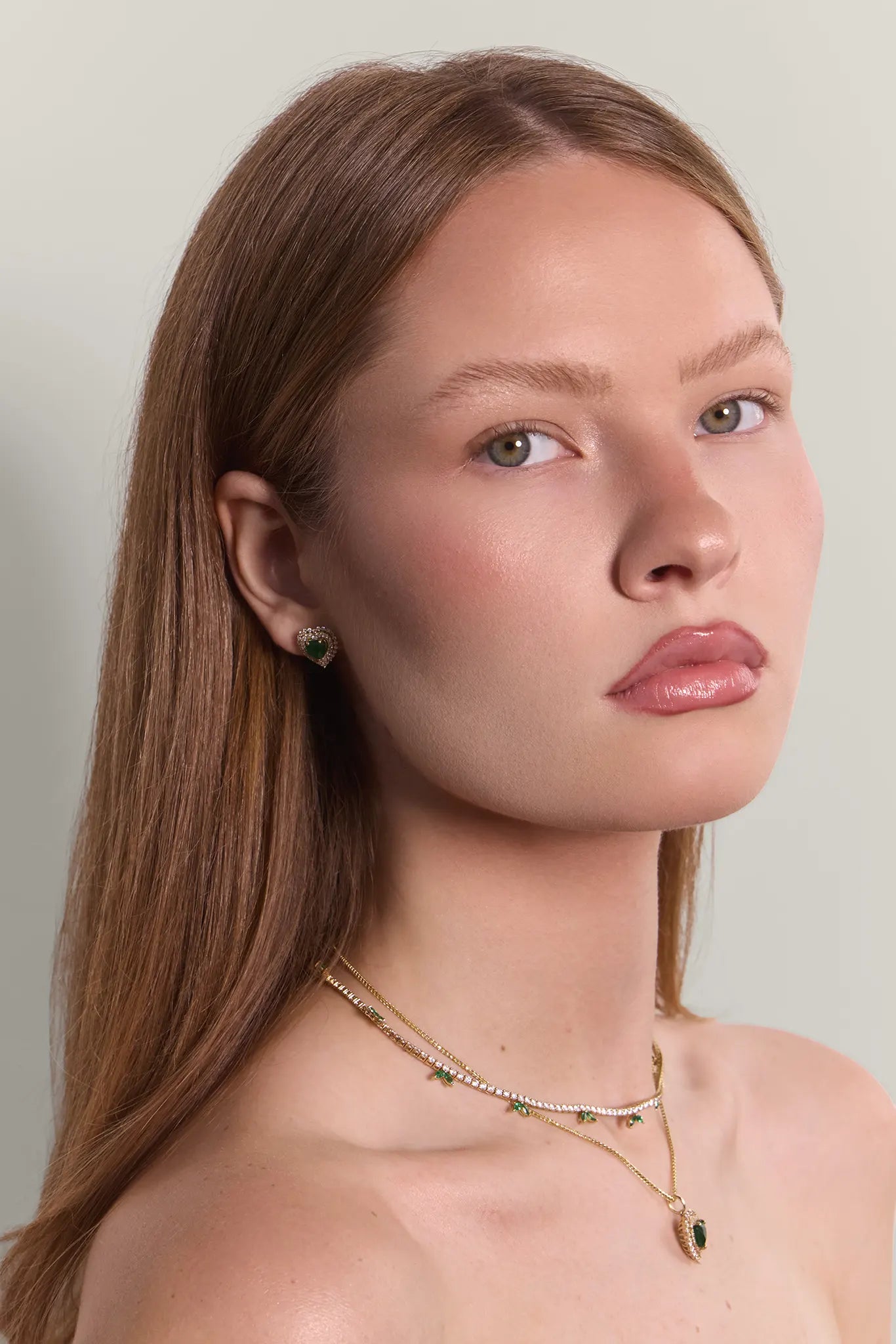 Woman wearing diamond and emerald necklaces with matching earrings against a neutral background