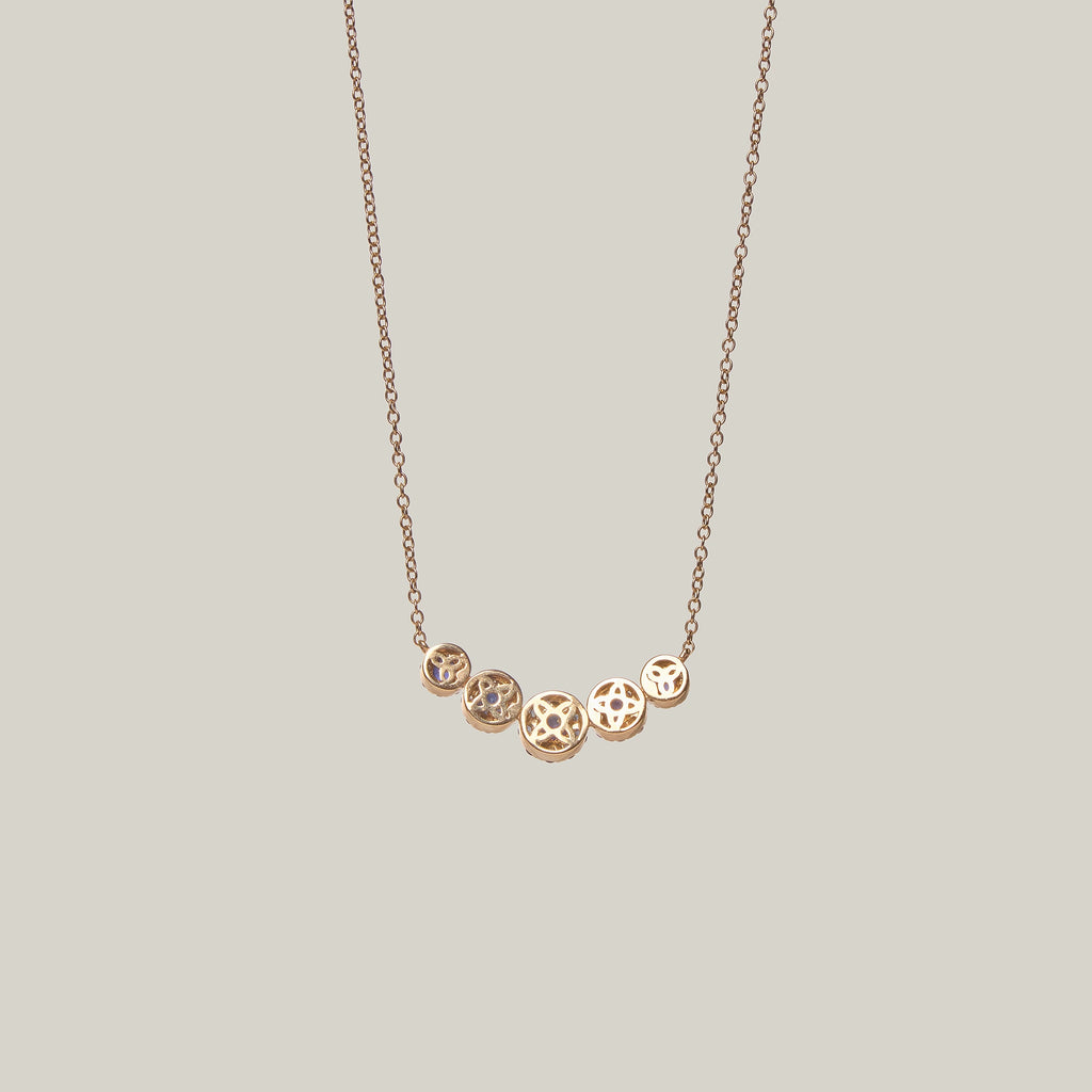 Rear view of a gold necklace with blue sapphires and diamonds on a light gray background