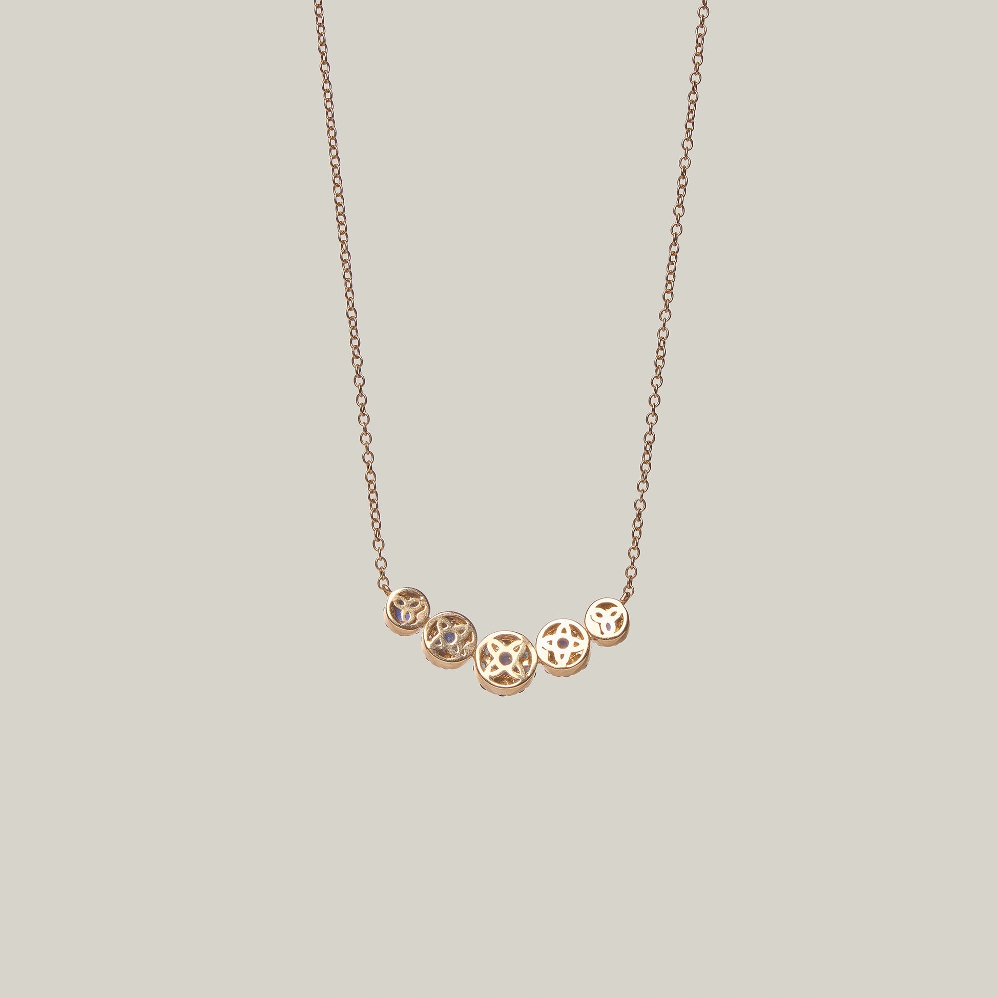 Rear view of a gold necklace with blue sapphires and diamonds on a light gray background