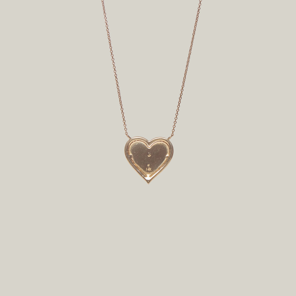 Close up rear view of a gold heart-shaped pendant with a diamond encrusted center and border on a light gray background
