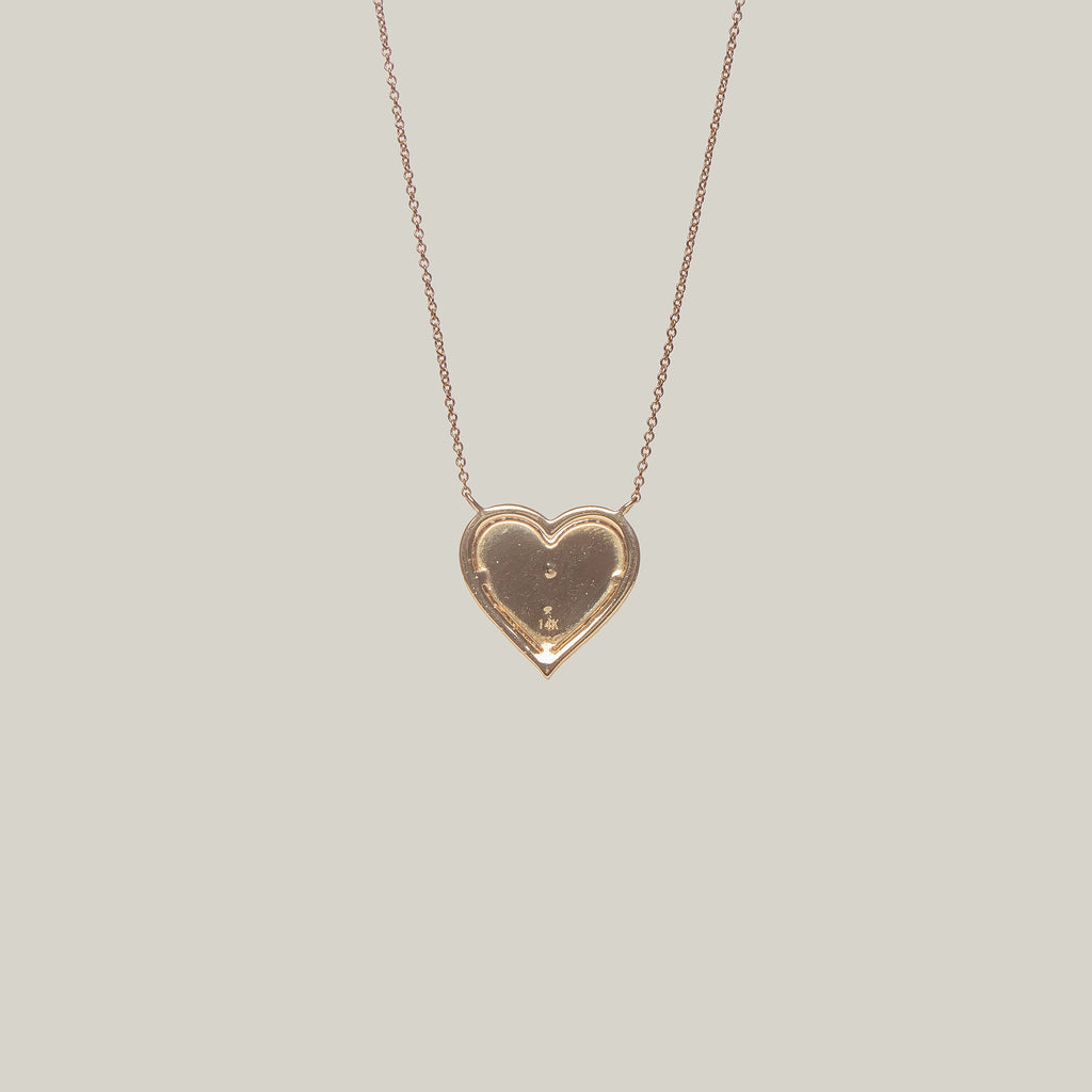Close up rear view of a gold heart-shaped pendant with a diamond encrusted center and border on a light gray background