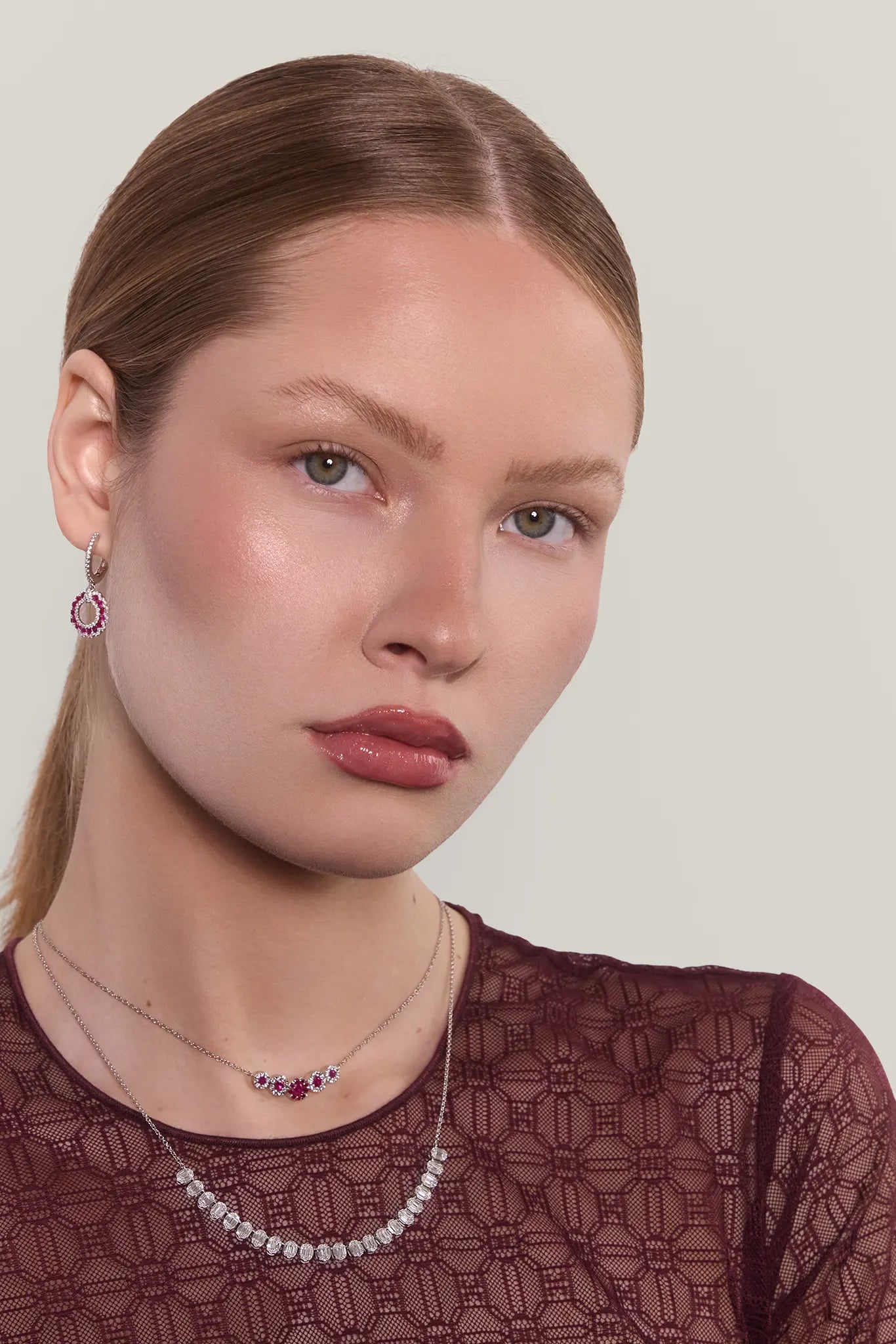 Woman wearing two necklaces and earrings with a neutral background