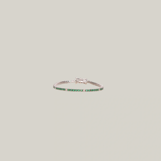 A tennis bracelet with diamonds and emeralds on a light gray background