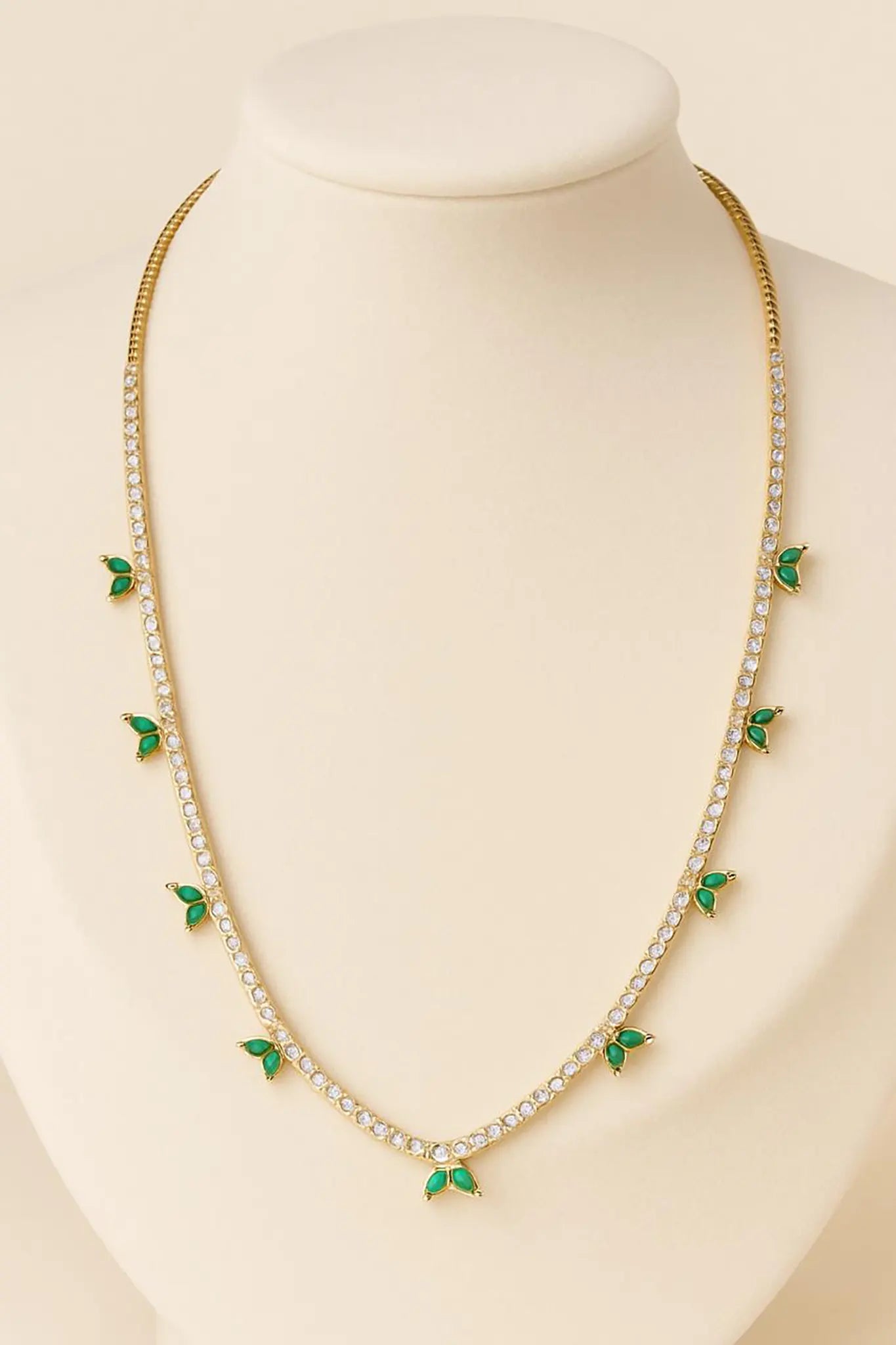 A diamond tennis necklace with emerald accents on a white bust