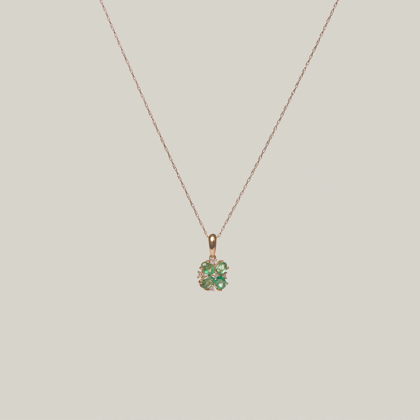 Close-up front-facing view of a gold necklace with a green four leaf clover pendant on a light gray background