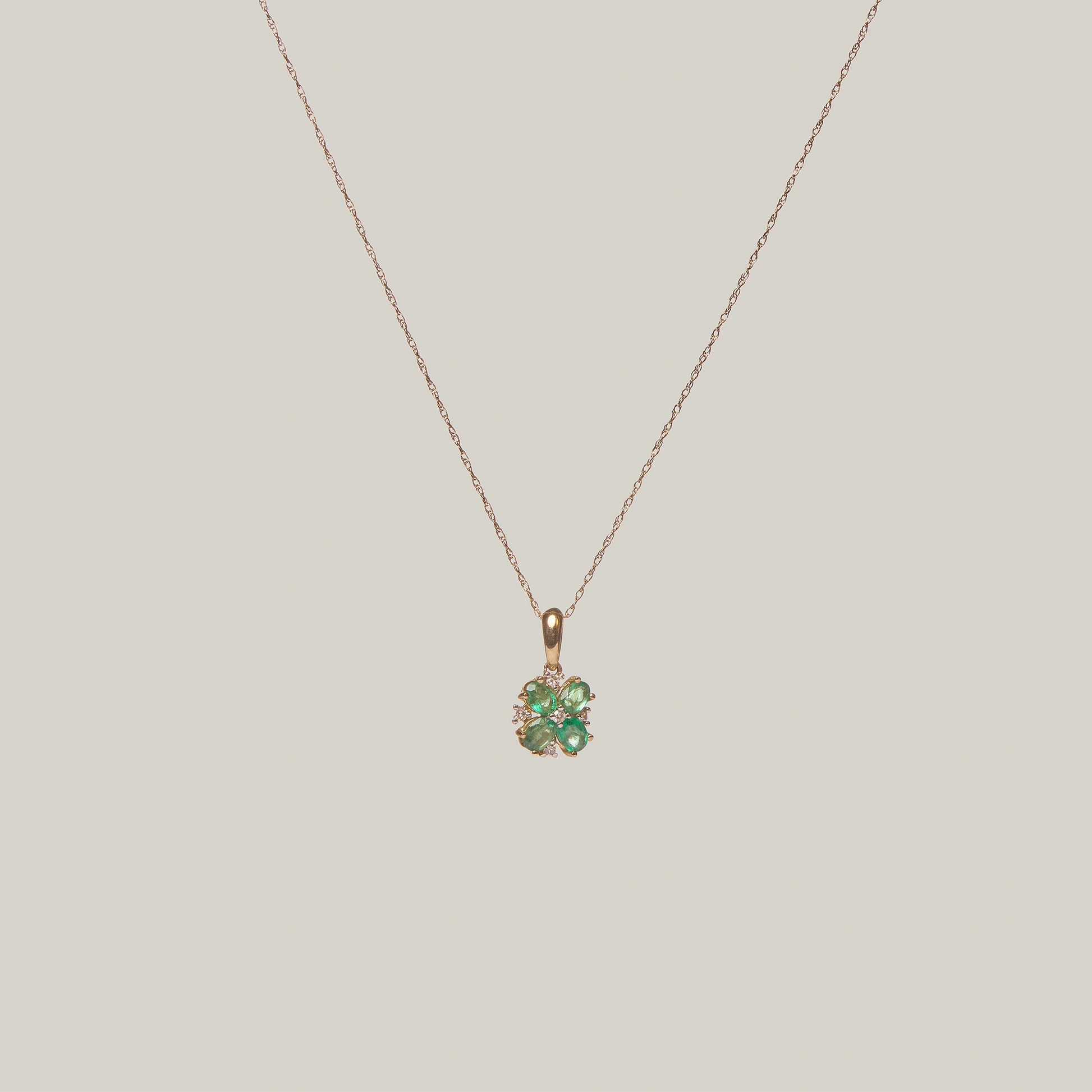 Close-up front-facing view of a gold necklace with a green four leaf clover pendant on a light gray background