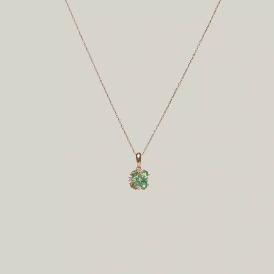 Close-up front-facing view of a gold necklace with a green four leaf clover pendant on a light gray background