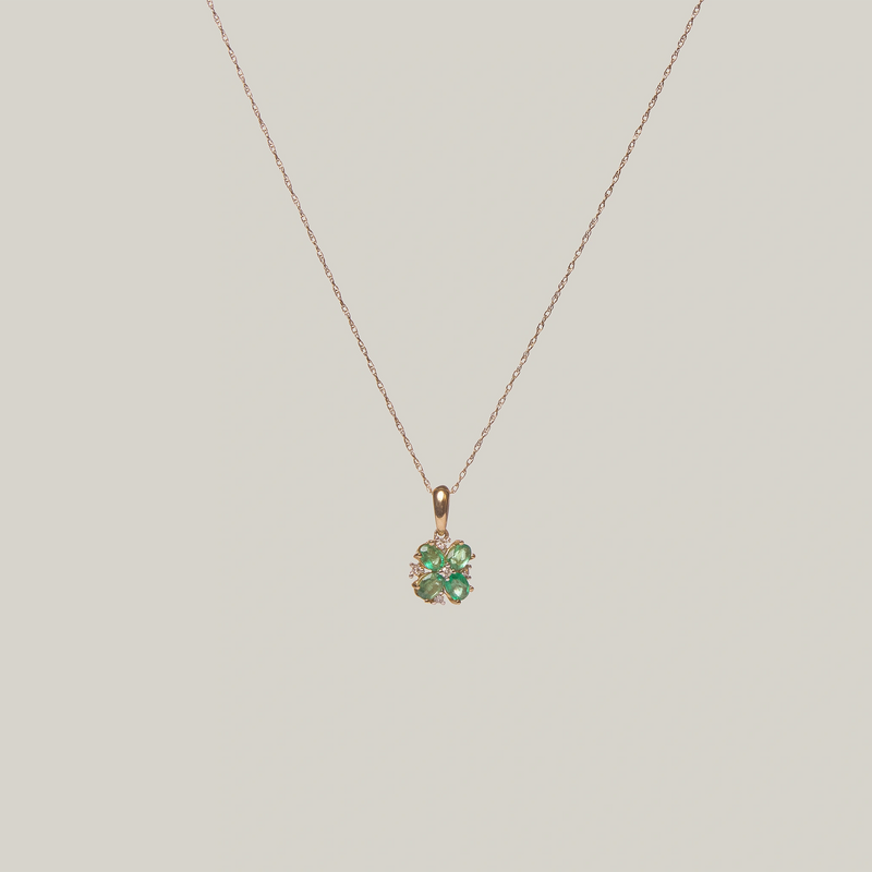 Close-up front-facing view of a green four leaf clover pendant on a light gray background