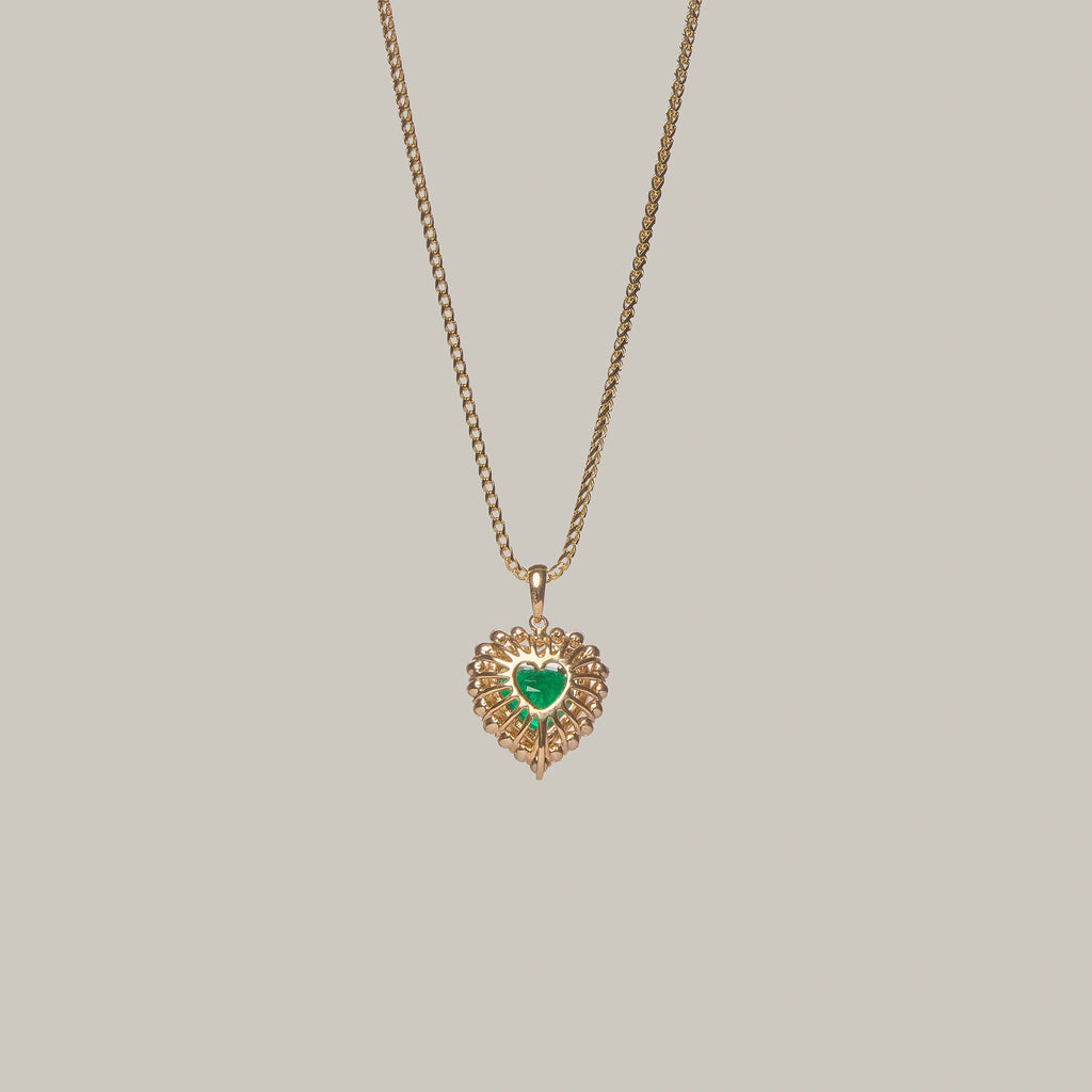 Rear-facing close-up of a heart-shaped emerald pendant on a light gray background