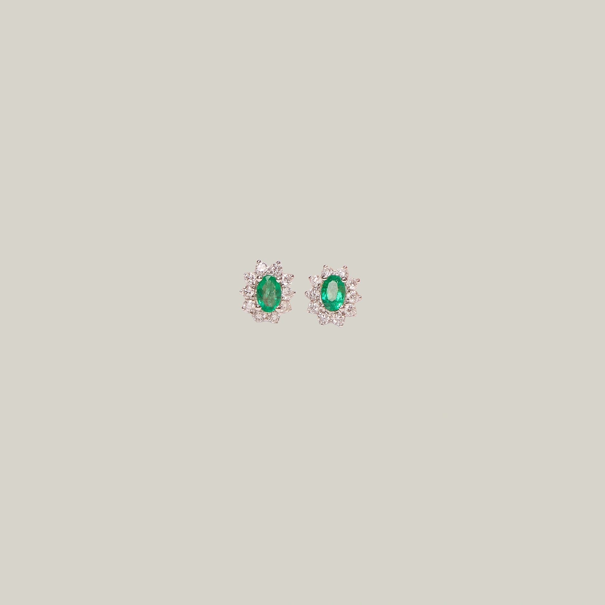 Pair of emerald and diamond stud earrings on a light gray background