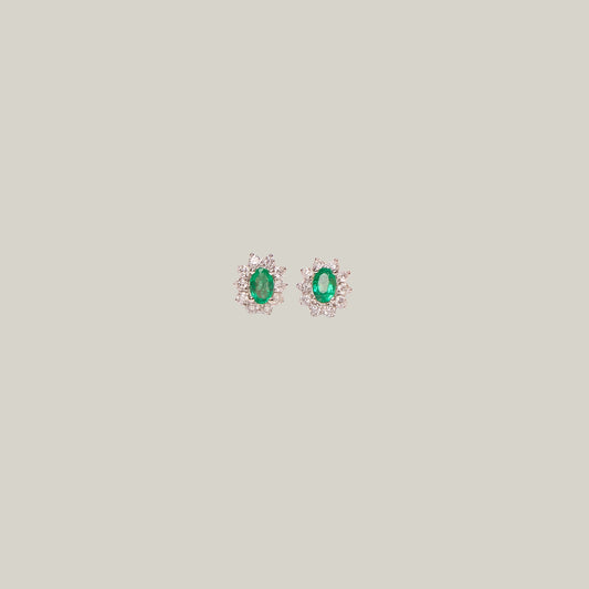 Pair of emerald and diamond stud earrings on a light gray background