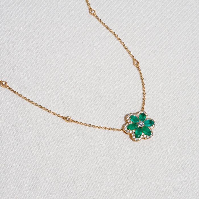An 18K gold emerald flower pendant with a center diamond, displayed against a light background.