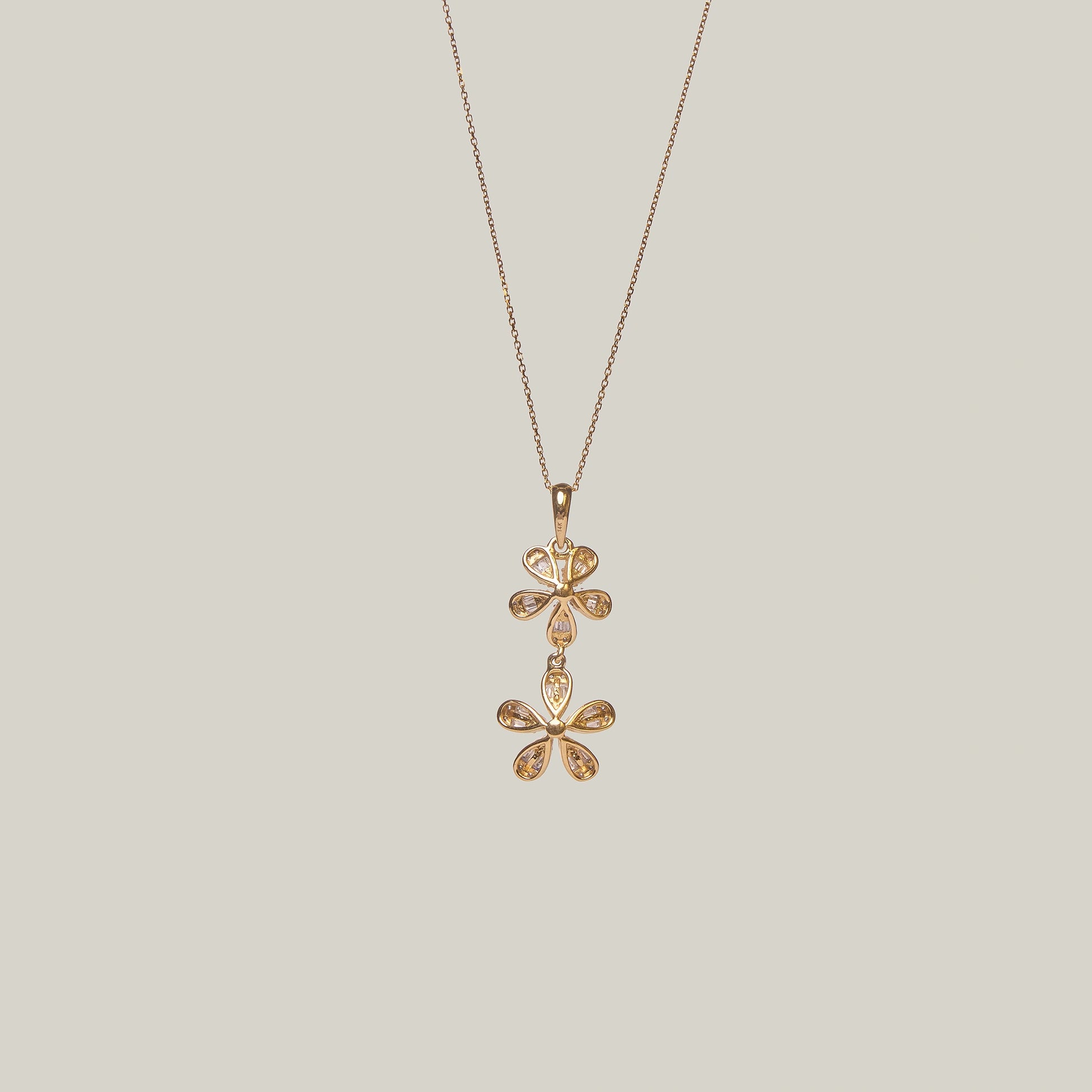 Close-up rear-facing view of a gold double flower diamond necklace on a light gray background