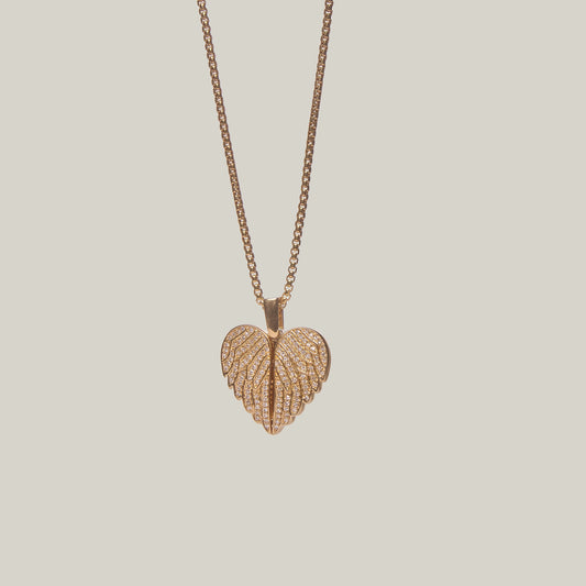 Close-up front-facing view of a gold heart shaped necklace with an angel wings design, encrusted with diamonds, on a light gray background