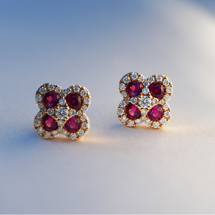 A pair of gold, ruby and diamond earrings featuring four red stones, a central diamond and pave set gems against a white background.