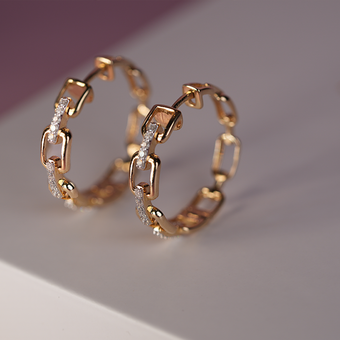 Side view of a pair of gold and diamond earrings with interlocking links against a pink and white background.