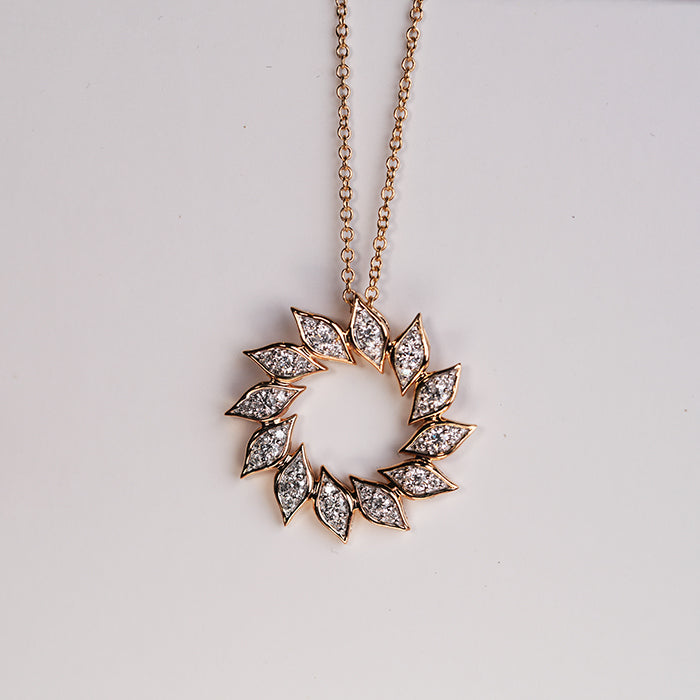 Close up view of a gold diamond pendant in a halo shape, suspended on a chain against a white background.