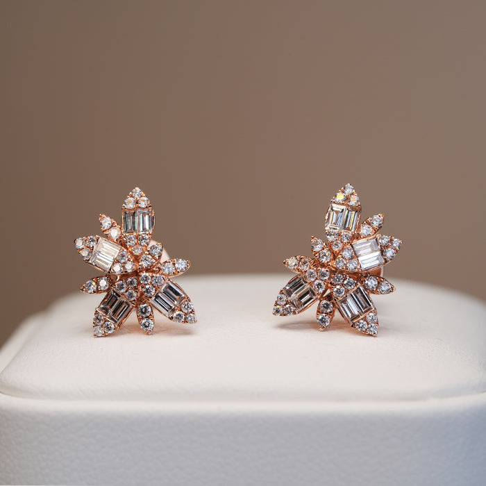 A pair of gold and diamond earrings with a textured pattern of pave-set and baguette cut stones on a white stand against a neutral background.