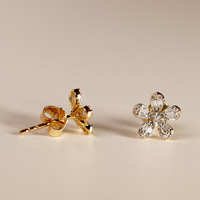 A pair of gold diamond flower stud earrings showcasing the front and side view against a neutral background.