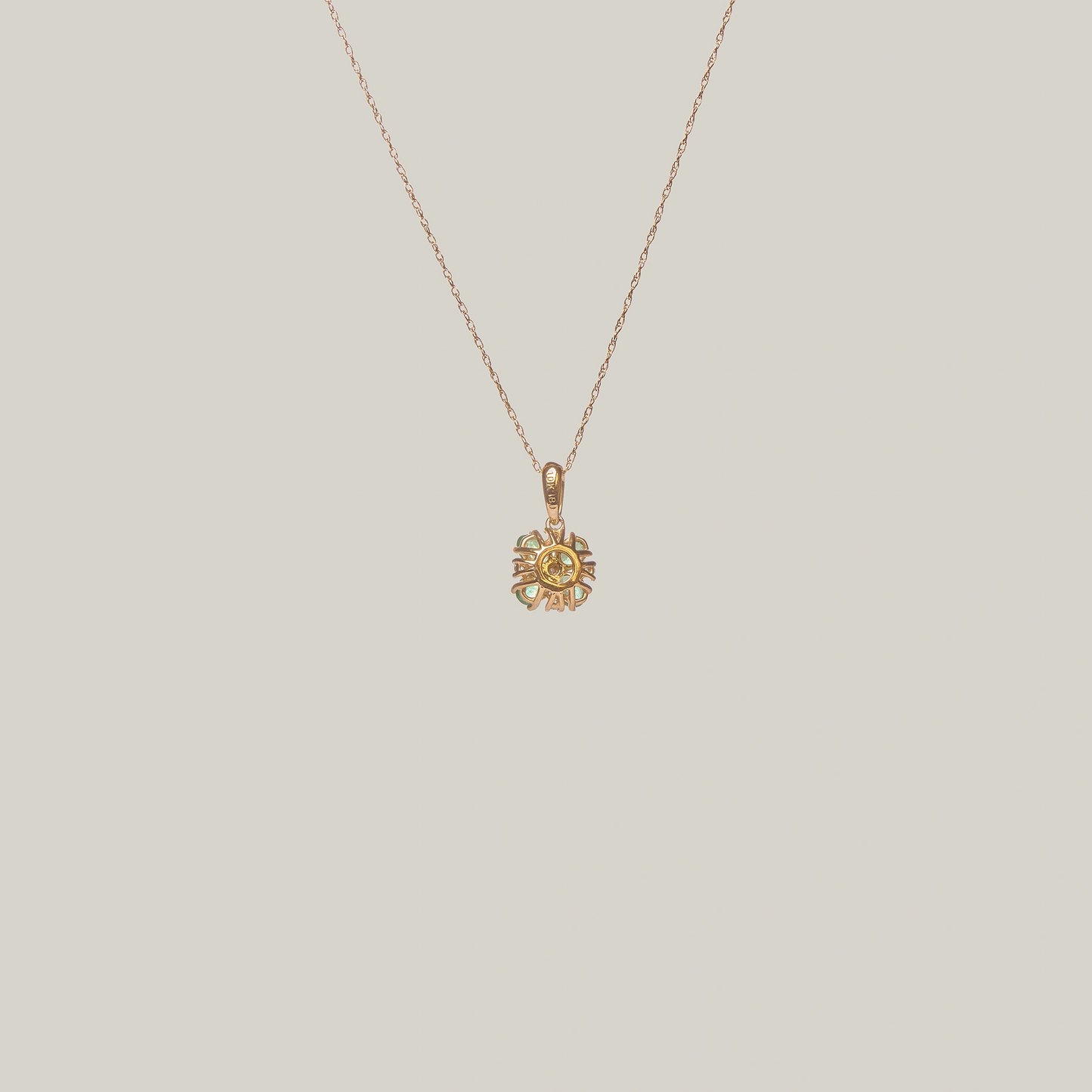Close-up rear-facing view of a gold necklace with a green four leaf clover pendant on a light gray background
