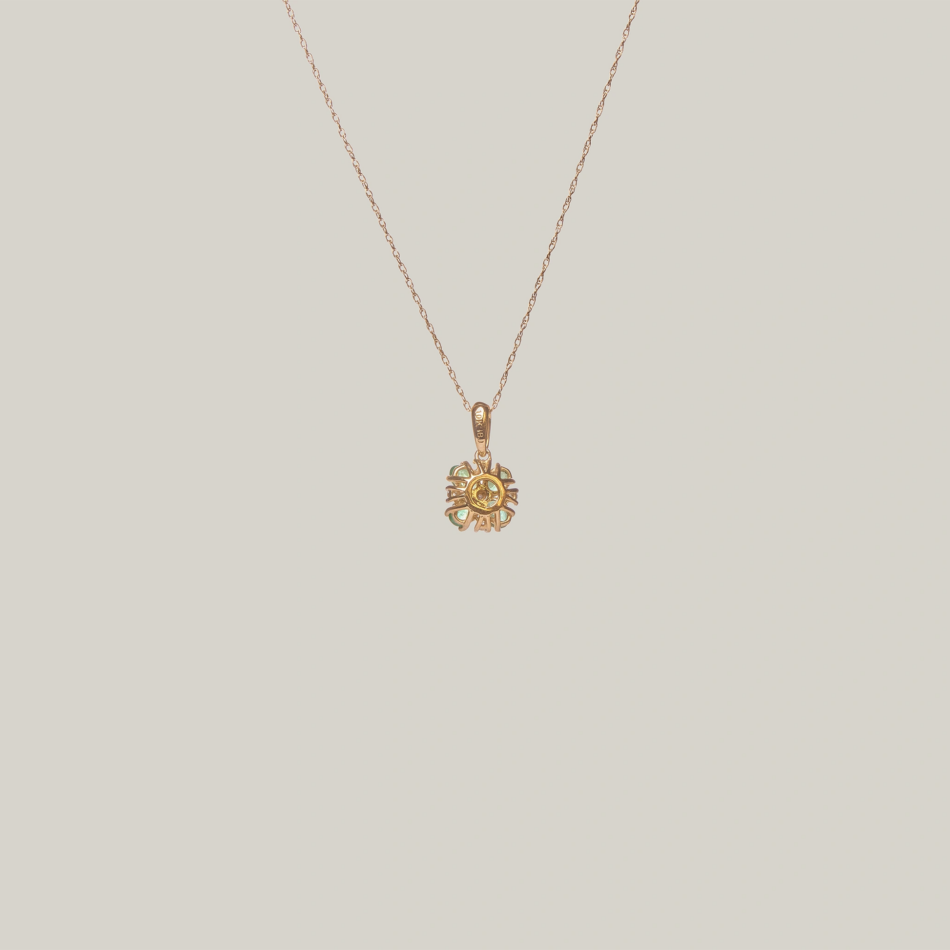 Close-up rear-facing view of a gold necklace with a green four leaf clover pendant on a light gray background