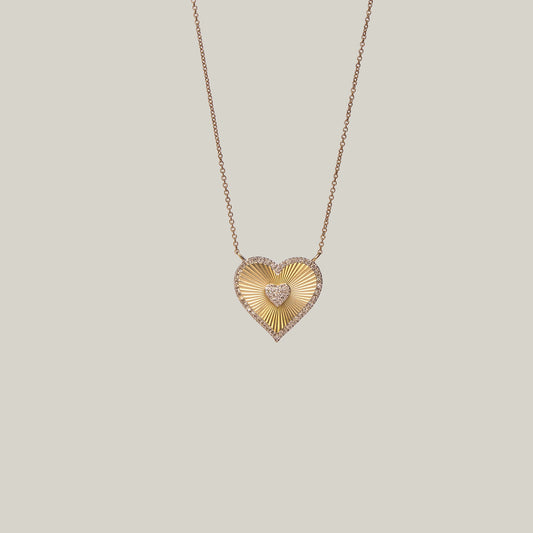 Close up front view of a gold heart-shaped necklace with a diamond encrusted center and border on a light gray background