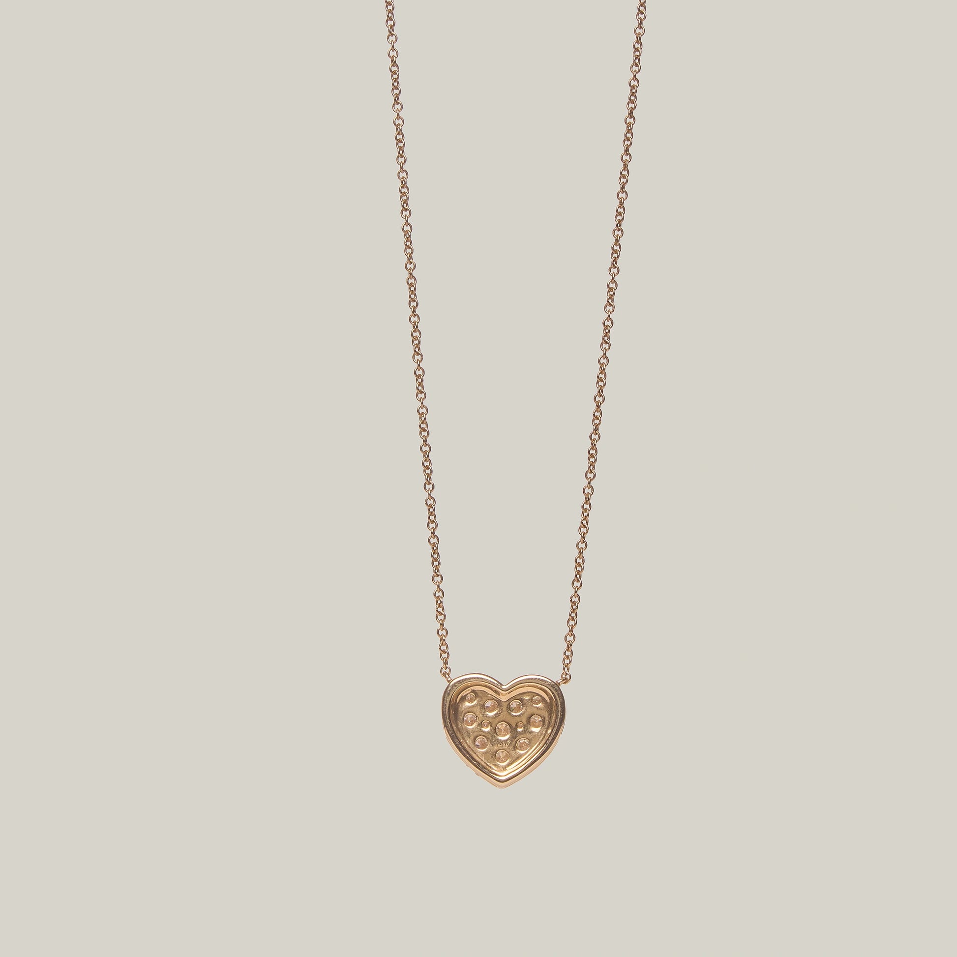 Close-up rear-facing view of a gold heart shaped diamond necklace on a light gray background.