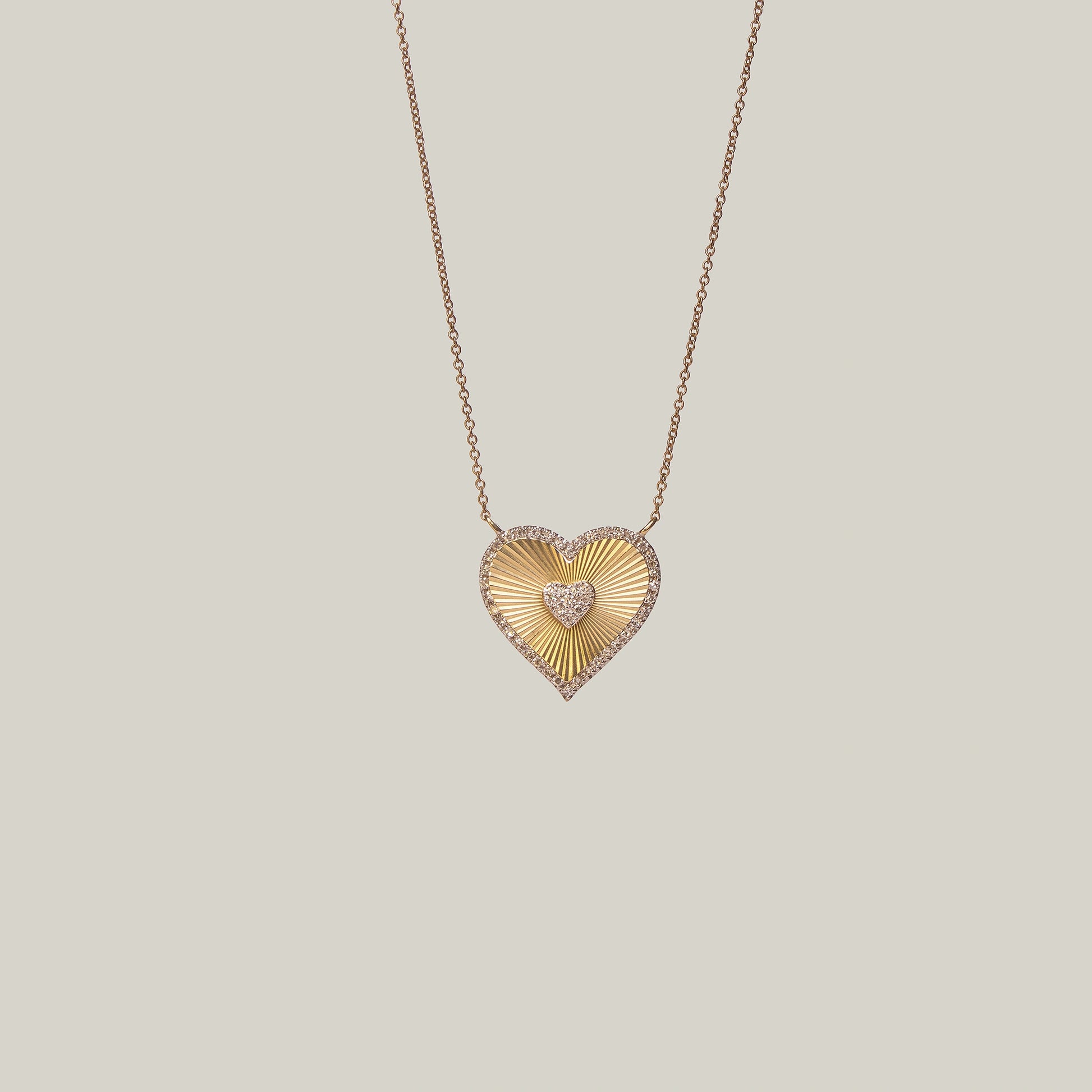 Close up front view of a gold heart-shaped pendant with a diamond encrusted center and border on a light gray background