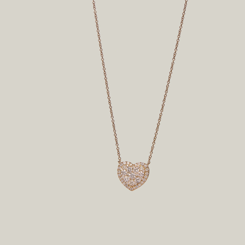 Close-up front-facing view of a gold heart shaped diamond pendant on a light gray background.
