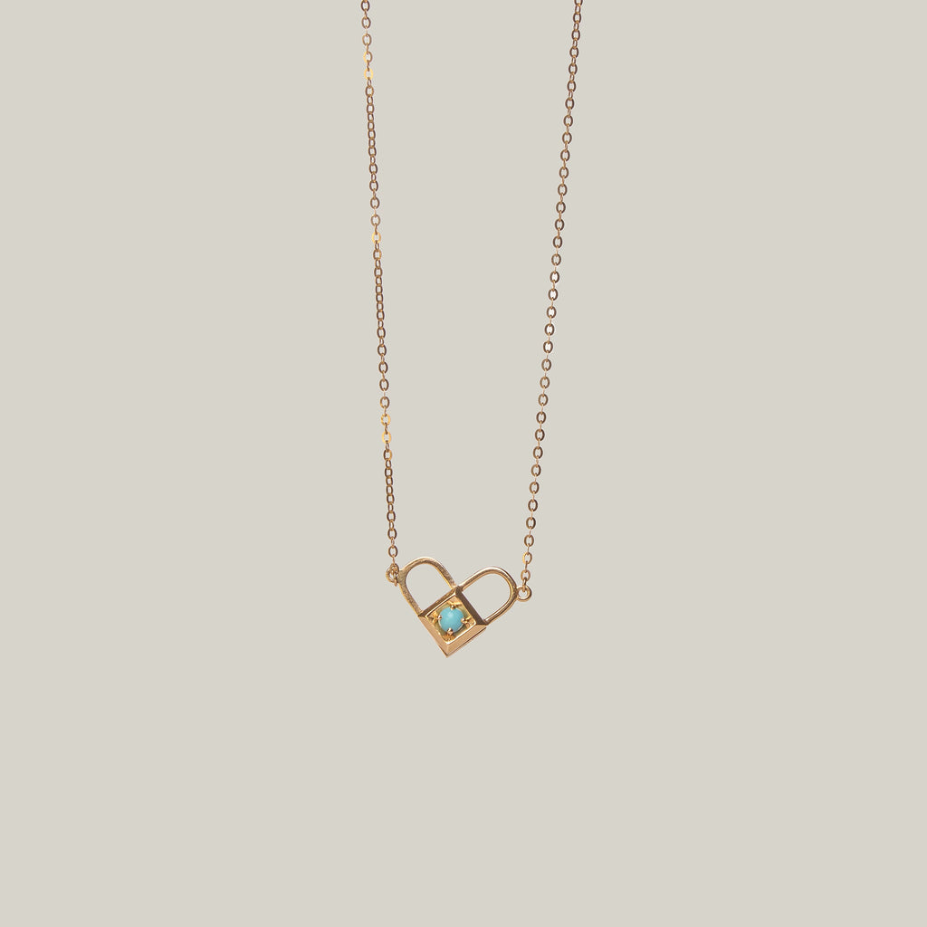 Close-up rear-facing view of an opened gold and turquoise padlock pendant with heart shape on a light gray background