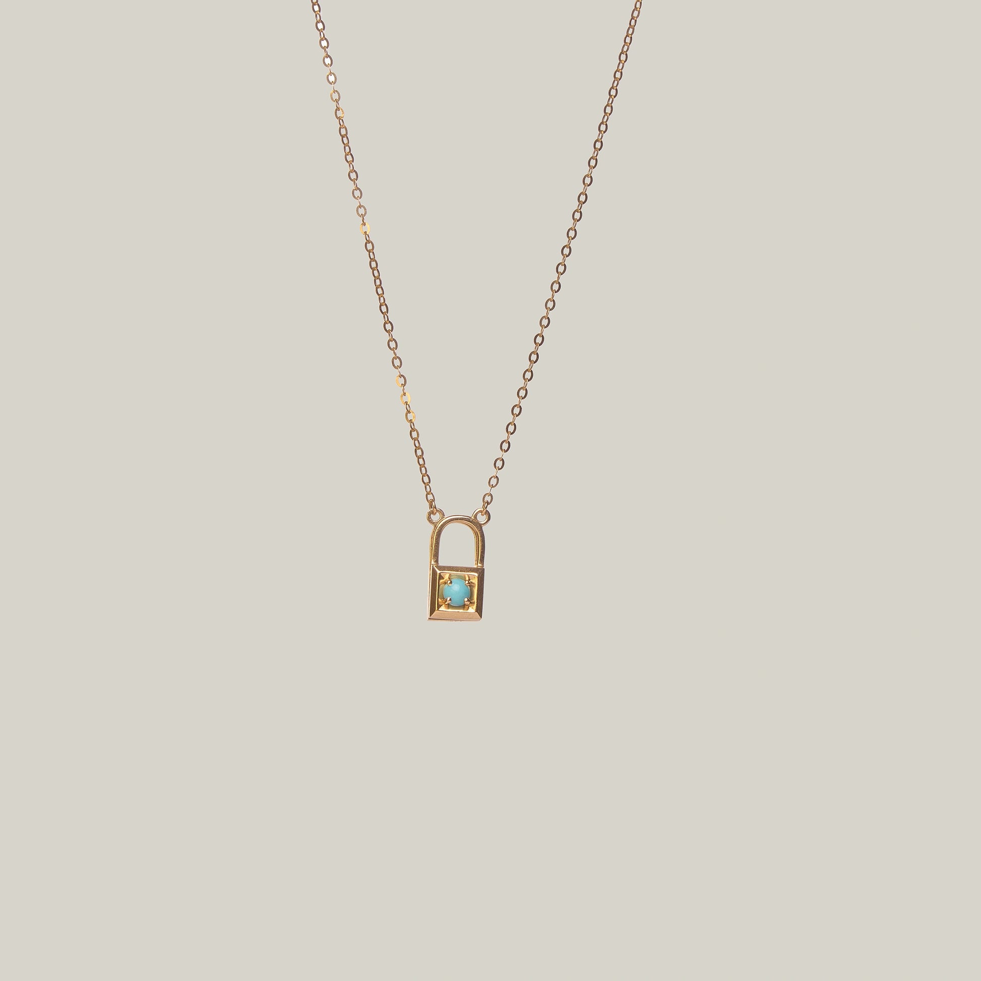 Close-up rear-facing view of a gold and turquoise padlock necklace on a light gray background