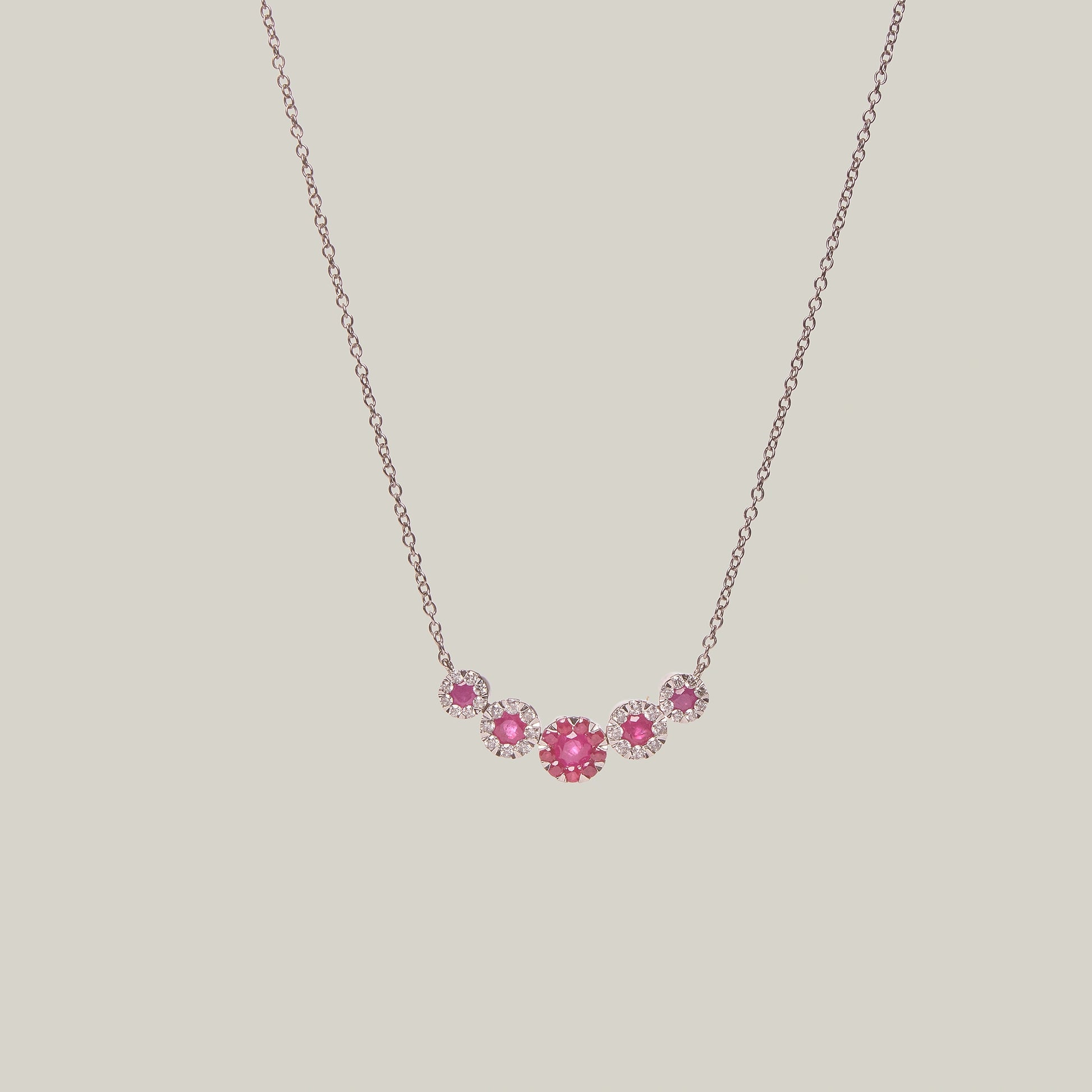 Gold necklace with rubies in a curved pattern on a light gray background