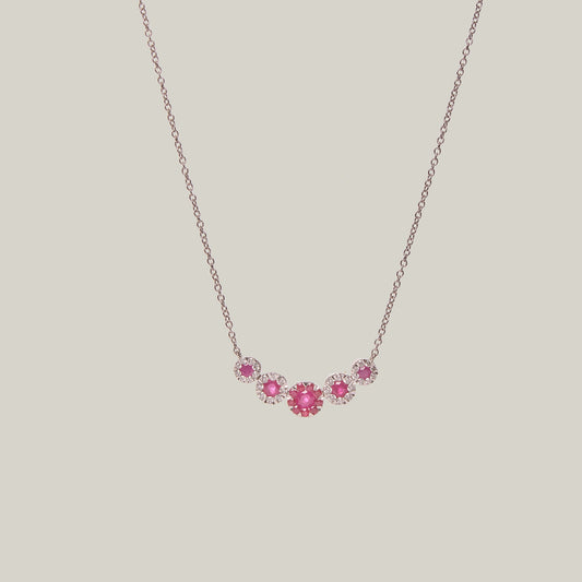 Gold necklace with rubies in a curved pattern on a light gray background
