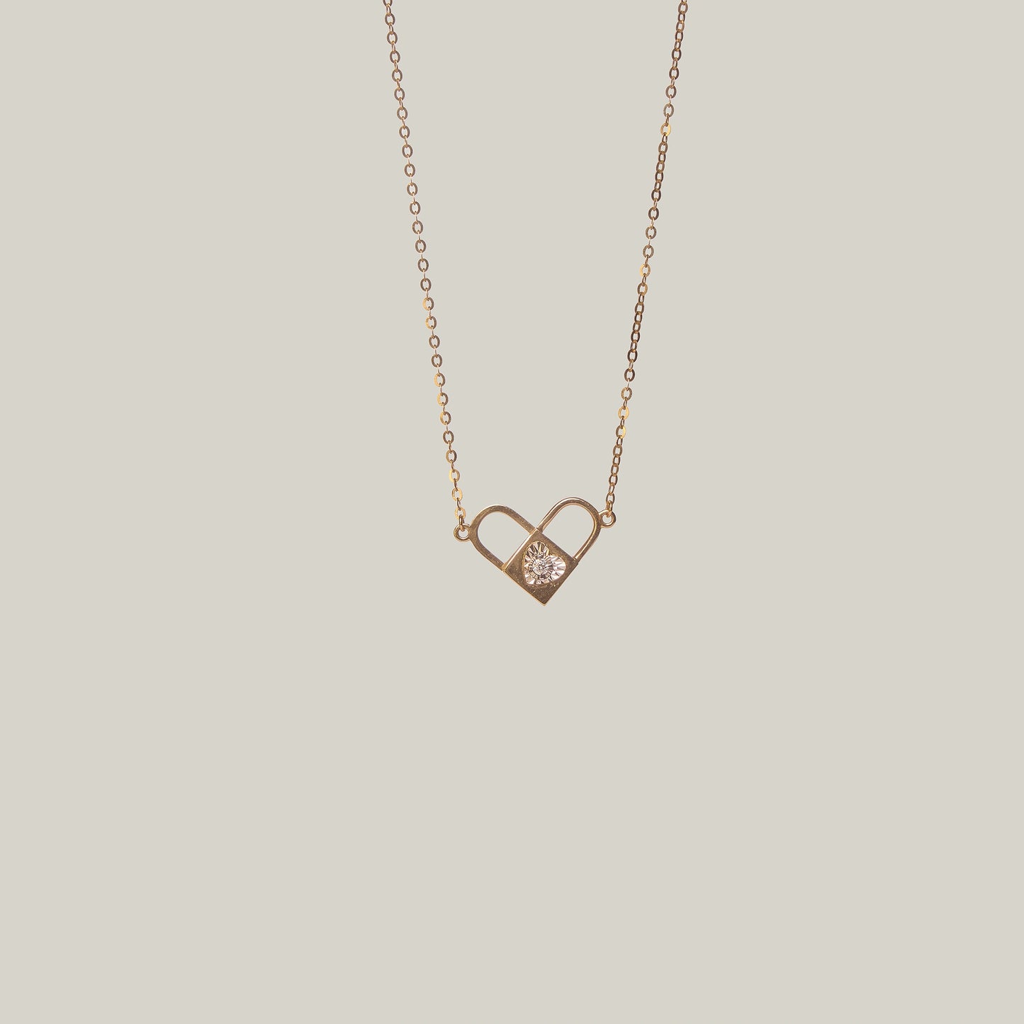Close-up front-facing view of an opened gold and diamond padlock necklace with heart shape on a light gray background