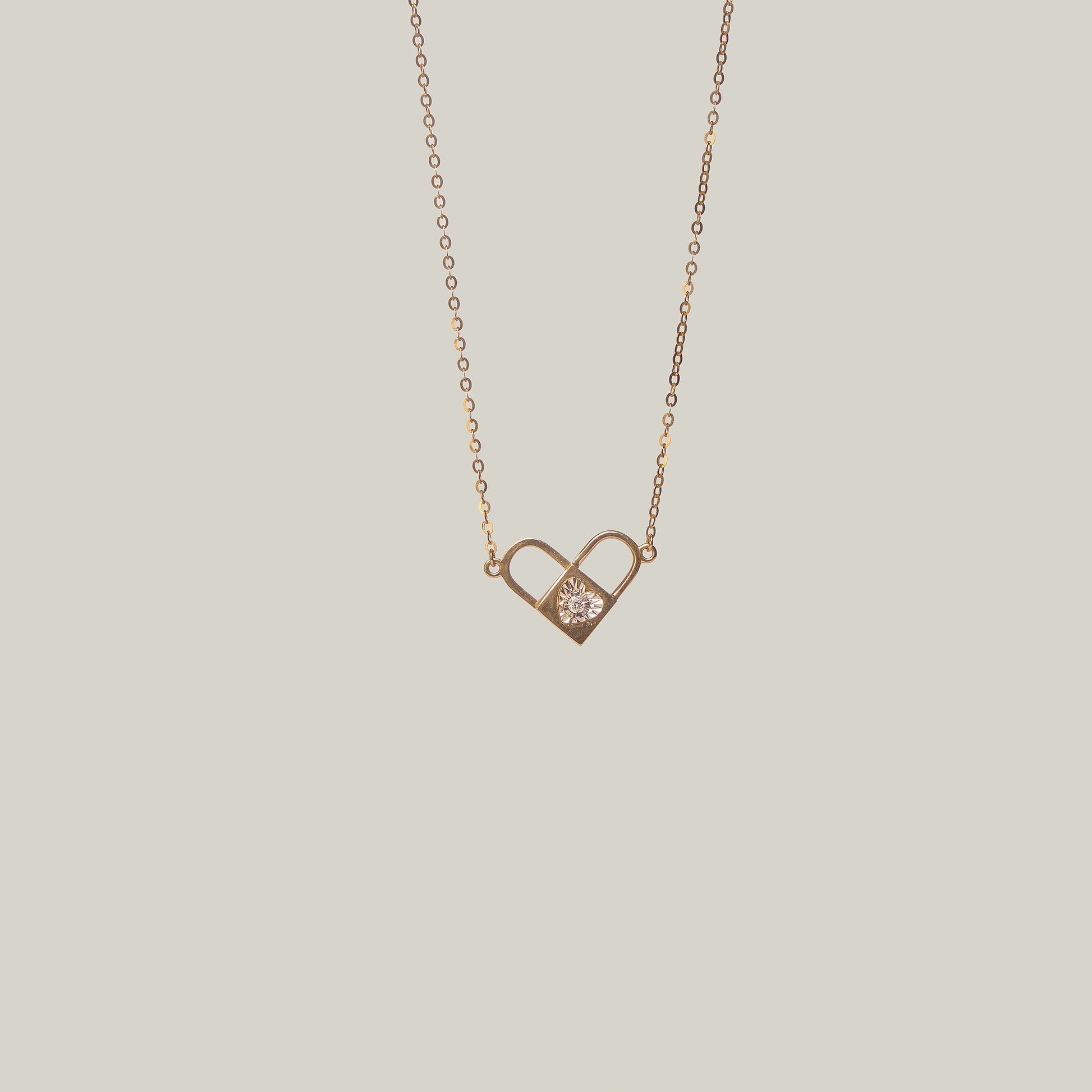 Close-up front-facing view of an opened gold and diamond padlock necklace with heart shape on a light gray background