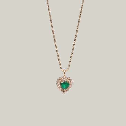 Front-facing close-up of a gold necklace with a heart-shaped emerald pendant on a light gray background