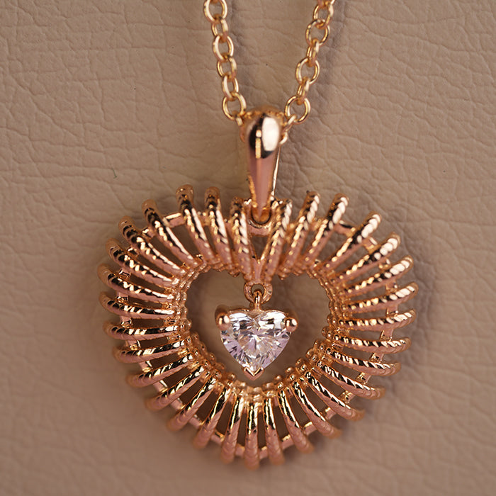 A gold heart-shaped pendant with a central diamond, attached to a necklace cord and displayed against a textured cream background.